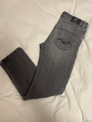 Grå Replay jeans straight fit - Säljer ett par grå jeans från Replay i rak modell. Jeansen har klassisk femficksdesign, svarta detaljer på bakfickorna och normal midja. Materialet är mjukt jeans-tyg som ger en avslappnad vibe. Perfekta till sneakers och hoodie.