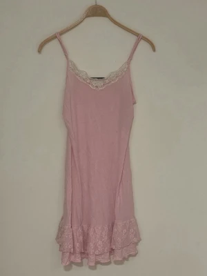 Rosa spetsdetaljerad klänning Gina Tricot - Söt ljusrosa klänning från Gina Tricot med tunna axelband, spetskant vid urringningen och volang med spets längst ner. Klänningen har en feminin och romantisk look, perfekt som sov plagg eller när du vill ha det extra mysigt