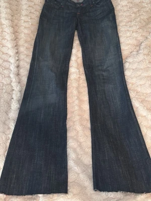 Rock & Republic bootcut jeans blå - Mörkblå jeans från Rock & Republic med bootcut passform. Snygga röda kontrastsömmar och broderad bakficka med stort R. Klassisk femficksmodell i jeansmaterial, perfekta till sneakers eller boots.