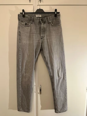 Grå jeans från Jack & Jones - Säljer ett par grå jeans från Jack & Jones med klassisk femficksdesign och raka ben. Jeansen har en snygg tvättad look och är tillverkade i slitstarkt bomullsmaterial. Passar perfekt till en avslappnad stil och har normal passform.