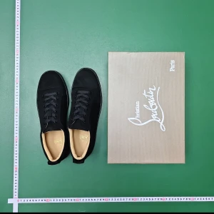 Svarta sneakers från Christian Louboutin - Säljer ett par svarta sneakers från Christian Louboutin i storlek 45. Skorna har en stilren design med rund tå, snörning och platt sula. Ovandelen är i mjuk mocka och insidan är beige. Yttersulan är röd, vilket är Louboutins signatur. Box medföljer.