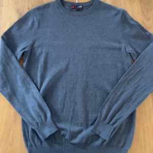 Grå bomullströja från Dressmann - Säljer en stilren grå tröja från Dressmann i mjuk pima bomull. Tröjan har rund halsringning, långa ärmar och ribbade muddar vid ärmslut och nederkant. Perfekt för lager-på-lager och enkel att matcha med jeans eller chinos.