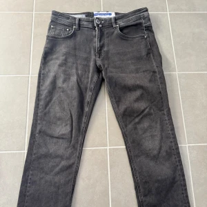 Svarta jeans från Jacob Cohën - Snygga svarta jeans från Jacob Cohën med klassisk femficksdesign och diskret logga på myntfickan. Jeansen har raka ben och normal passform, tillverkade i mjukt denimtyg med snygg tvättad look. Perfekta för dig som gillar stilrena och tidlösa jeans. Storlek 32x25.