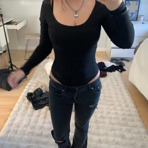 Svart ribbad body - Säljer en svart, tight och ribbad långärmad topp med rundad urringning. Toppen är figurnära och har en enkel, stilren look som passar till mycket. Materialet är stretchigt och bekvämt, perfekt för dig som gillar en clean och snygg stil.