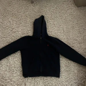 Polo Ralph lauren - En mörk blå Ralph lauren hoddie i storlek L. Den är i mycket bra skick och det finns inga tecken på användning. Priset kan diskuteras. Den ser svart ut Pga ljuset men den är Mörk blå. 14-16 år