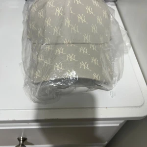 Beige New Era NY keps med monogram - Snygg beige keps från New Era med NY Yankees monogram över hela kepsen. Modellen är 9FORTY och har justerbar passform. Perfekt för dig som gillar sportig streetstyle och vill sticka ut med en unik design.