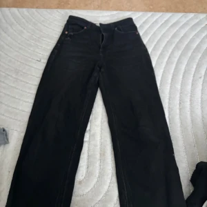 Svarta raka jeans - Säljer ett par svarta jeans med rak passform och klassisk femficksdesign. Byxorna har hög midja och är tillverkade i ett robust jeanstyg. Perfekta för dig som gillar en tidlös och clean look. Petite längd