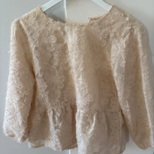 Beige blus med volang - Supersöt beige blus med volang nertill och struktur av blommor, nästan oanvänd