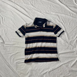 Randig pikétröja från Dressmann M - Snygg randig pikétröja från Dressmann i marinblått, vitt och beige med. Tillverkad i mjuk bomull som känns skön mot huden. Storleken är M. Annars inga konstigheter