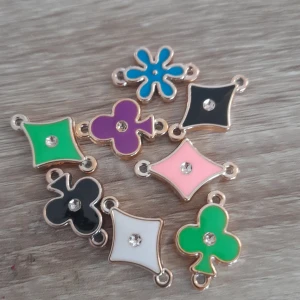 Färgglada berlocker med kristall - Säljer ett set med sju berlocker i olika former och färger, perfekta till armband eller halsband. Berlockerna har detaljer i guld och en liten kristall i mitten. Färgerna är blå, grön, svart, vit, rosa och lila. Formerna är inspirerade av spelkort och en blomma.