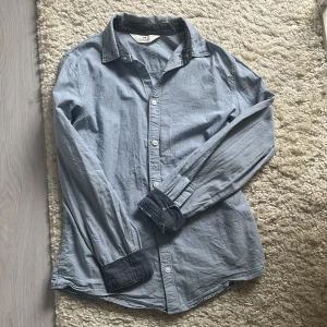 Ljusblå skjorta från H&M, strl 164 - Ljusblå skjorta från H&M i storlek 164. Skjortan har klassisk krage, vita knappar och kontrastfärgade mörkblå detaljer på insidan av krage och ärmslut. Inte så jätte ny men inte använt den den har mest tagit plats. Passar om man 160-175 runt där. Bara skriva för mer bilder eller frågor.😊
