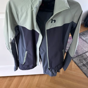 Grå täckbyxor från Hannah - Snygga täckbyxor från Hannah i olika grå nyanser med elastisk midja och logga baktill. Byxorna är tillverkade i ett slitstarkt syntetmaterial som passar perfekt för utomhusaktiviteter under kyligare säsonger.