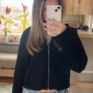 Svart kofta/jacka med dragkedja - Svart kofta med lång ärm och hel dragkedja framtill, nästan lite som en tun jacka. Tröjan är en enkel och clean , perfekt till jeans. Den har även två diskreta fickor fram till. Snygg att styla lager på lager.