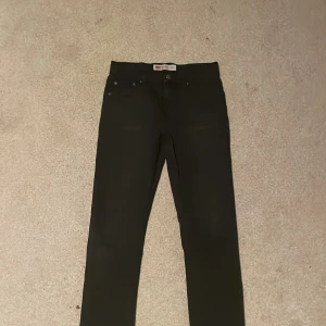 Svarta Levi's 512 Slim Taper jeans - Svarta jeans från Levi's modell 512 Slim Taper med klassisk femficksdesign och knappstängning. Jeansen har smal passform med avsmalnande ben och är tillverkade i mjukt bomullsmaterial med lite stretch för extra komfort. Perfekt för dig som gillar stilrena och moderna jeans.