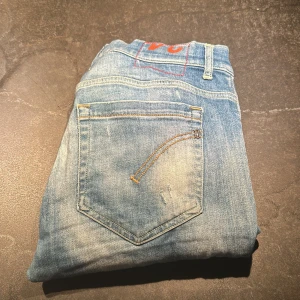Blå skinny jeans från Dondup - Säljer ett par ljusblå skinny jeans från Dondup, modell George Skinny Fit. Jeansen har slitna detaljer och en snygg tvätt med ljusa partier. Klassisk femficksdesign och tillverkade i jeansmaterial. Perfekta för dig som gillar en smal passform och italiensk design.