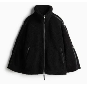 Svart teddyjacka med dragkedja - Mysig svart teddyjacka med hög krage och hel dragkedja framtill. Jackan har två fickor och en oversized passform som ger en chill vibe. Perfekt för kalla dagar när du vill vara både varm och snygg.