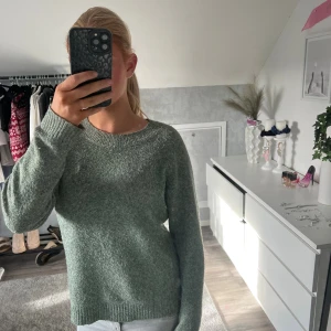 Grön stickad tröja med rund hals - Säljer en mjuk och skön grön stickad tröja med rundad halsringning och långa ärmar. Perfekt för dig som gillar enkel och stilren design. Tröjan har ribbade muddar vid ärmslut och nederkant för extra komfort. Passar till jeans eller kjol.