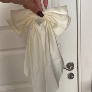 Vit sidenrosett till håret - Superfin vit rosett i glansigt sidenmaterial med långa band. Fästs enkelt med metallspänne på baksidan. Perfekt accessoar för att lyfta din frisyr och ge en söt och elegant touch.