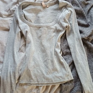 Ljusgrå ribbad topp från Nelly - Supersnygg ljusgrå ribbad topp från Nelly med lång ärm och bred, fyrkantig urringning. Toppen är figurnära och har en enkel, stilren look som passar perfekt till jeans eller kjol. Mjuk och stretchig i materialet för en bekväm känsla. Fråga!