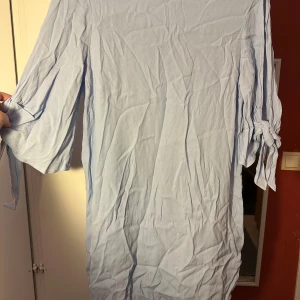 Ljusblå klänning med knytärm från H&M strl: 44 - Säljer en ljusblå klänning från H&M i storlek 44. Klänningen har trekvartsärmar med snygga knyt-detaljer vid ärmsluten och är tillverkad i ett mjukt, lätt material. Enkel och stilren design som är perfekt för dig som gillar minimalistiskt mode.