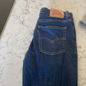 Levi's 512 Slim Taper jeans blå - Snygga Levi's 512 Slim Taper jeans i klassisk mörkblå denim med kontrastsömmar och fem fickor. Modellen har smal passform med avsmalnande ben och normal midja. Perfekta för dig som gillar en modern och stilren look. De är storlek 16a
