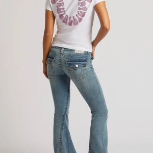 True Religion Joey Low Rise Flare Jeans - Säljer ett par blå True Religion Joey jeans med låg midja och rejäl utsvängd bootcut. Klassiska bakfickor med lock och silverknappar, samt tydliga sömmar. Jeansen är i denim och har en snygg tvättad look. Perfekta för dig som gillar retrovibbar och statement-jeans. Använda några gånger köptes i sommar. 