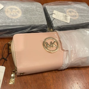 Rosa plånbok från Michael Kors - Väskorna är HELT NYA och aldrig använda. Den jag plockade ut var ROSA men finns även i SVART och MARIN BLÅ. Bara fråga om man vill ha fler bilder eller bild på någon specifik. Priset kommer vara 299kr/st.