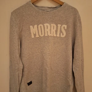 Grå sweatshirt från Morris i bomull - Grå sweatshirt från Morris med vit broderad logga framtill. Klassisk rund halsringning och långa ärmar. Tillverkad i mjuk bomull, perfekt för en chill och stilren look. Storlek medium.