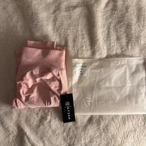 Rosa leggings från GTECH, storlek S - Snygga ljusrosa leggings från GTECH med hög midja och seamless design. Perfekta för träning eller chill, med stretchigt material som sitter skönt och formar sig efter kroppen. Diskret logga framtill i vitt och bred resår i midjan för extra support. Helt nya