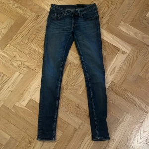 Tiger of Sweden Slender jeans blå - Snygga blå jeans från Tiger of Sweden i modellen Slender. De har en smal passform med klassisk femficksdesign och orangea kontrastsömmar. Jeansen är tillverkade i Italien och har en stilren, mörk tvätt som passar till det mesta.