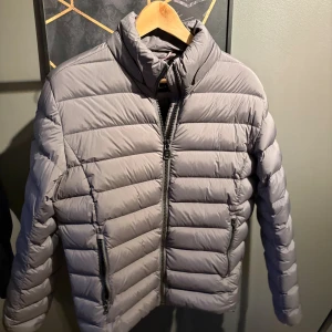 Grå dunjacka från Colmar, stl 50 - Säljer en grå dunjacka från Colmar i storlek 50 passar S/M. Jackan har quiltad design, hög krage och två dragkedjeförsedda fickor framtill. Perfekt för kyliga dagar och har en clean, modern look. Klassisk Colmar-logga på ärmen.