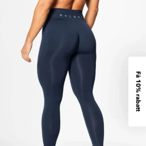 Blå träningsbyxor från Relode - Snygga mörkblå leggings från Relode med hög midja och tight passform. Perfekta för träning, tillverkade i stretchigt syntetmaterial som sitter skönt och formar benen. Diskret logga i midjan och stilren design utan synliga sömmar. Små noppror kan finnas.