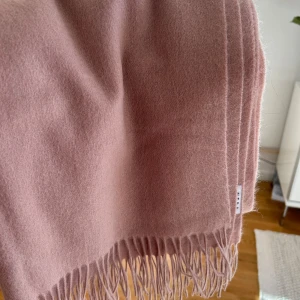 Ny Rosa halsduk i ull från Wera - Supermjuk och stilren halsduk från Wera i en ljusrosa ton. Halsduken är i ull och har klassiska fransar i kanterna. Perfekt accessoar för att lyfta din outfit under kyliga dagar.