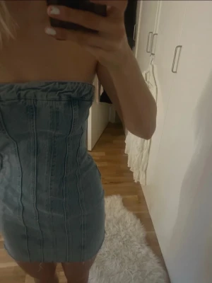 Jeansklänning från Zara  - Säljer en snygg jeansklänning från Zara i storlek XS. Klänningen är kort, axelbandslös och har en tight passform med markerade sömmar och rå kant nedtill. Prislappen kvar