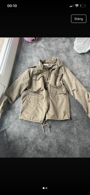 Beige overshirt från Dressmann XL - Säljer en beige overshirt från Dressmann i storlek XL. Jackan har dragkedja framtill, snörning i nederkant och fyra praktiska fickor med lock. Perfekt för dig som gillar en clean och avslappnad stil.