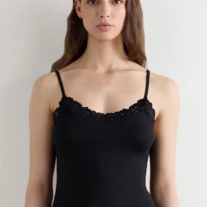 Svart spetskantad linnetopp Intimissimi - Svart linnetopp från Intimissimi med smala axelband och vacker spetskant längs halsringningen. Toppen är figurnära och har en mjuk, stretchig känsla. Perfekt att styla med jeans eller kjol för en clean look.