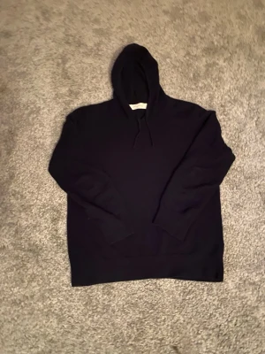 Mörk blå Kashmir hoodie från Sayless - Mjuk och stilren mörk blå hoodie från Sayless i kashmir. Klassisk modell med huva och dragsnören, ribbade muddar och lång ärm. Perfekt för dig som gillar en clean och enkel look