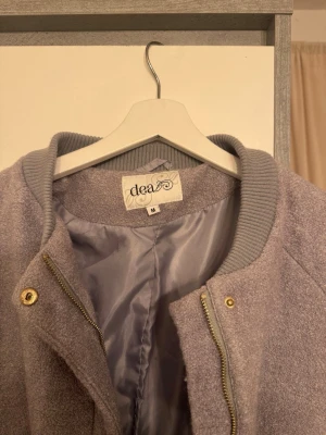 Beige ullkappa från Dea, storlek M - Säljer en beige kappa från Dea i storlek M. Jackan har en rak och loose passform, ribbad krage och stängs med både dragkedja och guldfärgade knappar. Materialet är ulligt och mjukt, perfekt för höst och vinter. Fickor på sidorna för extra chill vibe.