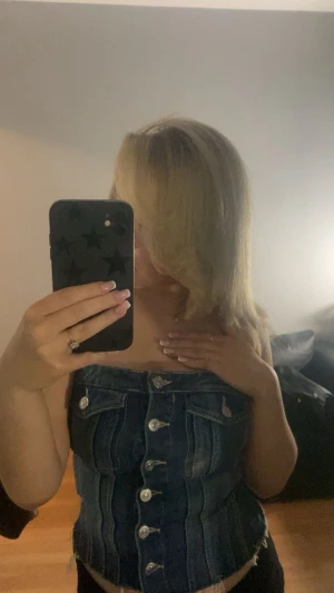 Mörkblå denim tubtopp med knappar - Säljer en snygg ZARA topp i mörkblå denim med silverfärgade knappar framtill. Toppen har en bandeauform och coola sömmar som ger en korsettliknande look. Perfekt för dig som gillar statement-plagg och vill sticka ut med en unik jeansstil.