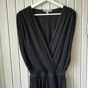 Svart byxdress / jumpsuit från House of Dagmar - Svart skräddad jumpsuit från House of Dagmar. Hög kvalitet med svensk design, smalare midja och snyggt fall i den vida byxan. Dolda små tryckknappar i sidan och framtill i den djupa veckade v-linjen i toppen. Vacker bred veckning över axlarna i den ärmlösa modellen. Styla med ett statement halsband och klackskor till fest eller med sneakers för en ledig look. Kolla in min profil  för fler jumpsuits!