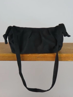 Axelbandsväska  - Axelbandsväska, perfekta vardagsväskan. Denna väskan är gjord av svarta jeans på utsidan och grönt möbeltyg på insidan. Innuti finns en ficka på ena sidan där du kan lägga småsaker och två små fickor på andra sidan. Stängningen sker med en lite knapp på insidan. Axelbandet är justerbart genom att knyta på olika sätt, som längst ca 80cm. 