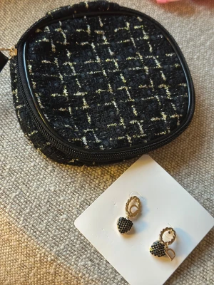 Gift Set Svart och guld rutig tweedväst - Snygg svart väst i tweed med rutigt mönster i guld. Västen har en klassisk form och är tillverkad i ett grovt, texturerat material som ger en lyxig känsla. Perfekt för att lyfta din outfit med lite extra edge och stil.