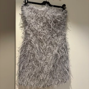 Silver glittrig kortklänning med fransar - Unik och trendig kortklänning i silver med glittriga detaljer och massor av fransar som ger en cool textur. Klänningen är axelbandslös och har en festlig vibe med sitt skimrande material PERFEKT till nyår.