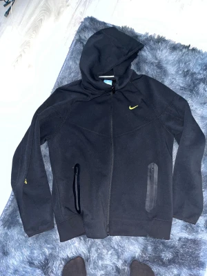 Nocta Nike Huvtröja  M Svart - Nocta Nike huvtröja för herrar i storlek M. Tröjan är svart och har huva samt dragkedja framtill. Materialet är mjukt och anpassat för olika sportaktiviteter inom övriga sporter.