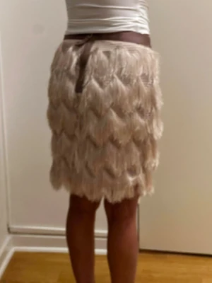 Beige fransig kortkjol med volang - Säljer en beige kortkjol med flera lager fransar som ger en cool och unik look. Kjolen har volangdetaljer och ett brett midjeband i mörkare beige ton. Perfekt för dig som vill sticka ut med en trendig och lekfull stil.