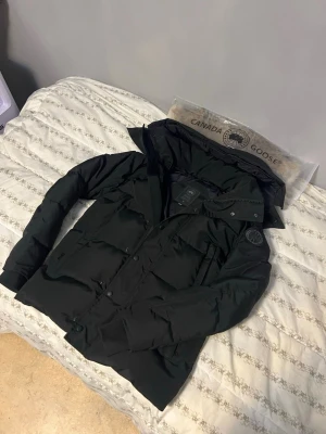 Canada Goose wyndham  - Canada Goose wyndham jacka med klassisk patch på ärmen. Jackan har flera fickor med både dragkedja och knappar, samt ribbade muddar vid ärmslut. Materialet är slitstark polyester och dunfyllning för extra värme. Perfekt för kalla vinterdagar.Trots det så är den oanvänd inga hål ingen skada alls jackan är 100% frisk!