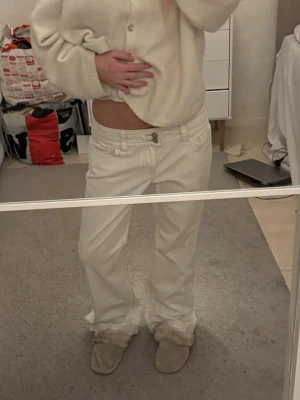 Vita bootcut jeans från Cabi - Säljer ett par vita jeans från Cabi med bootcut passform och låg midja. Byxorna har snygga detaljer med dubbla knappar fram, kontrastsömmar och bakfickor med dekorativ brodering och knappstängning. Materialet är kraftig bomull.💘