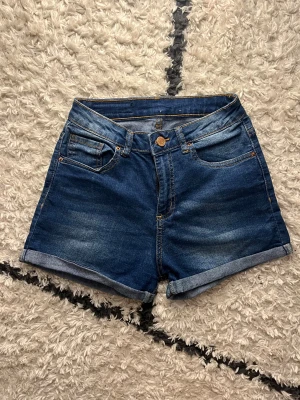 Blå denimshorts med uppvik - Snygga blå jeansshorts med klassisk femficksdesign och uppvikta benslut. High waisted och stretchiga 