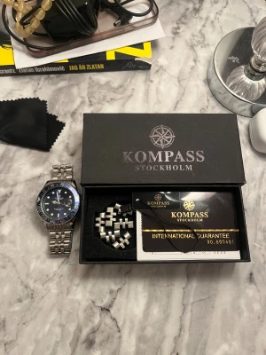 Kompass Stockholm blå klocka stål - Snygg armbandsklocka från Kompass Stockholm med blå urtavla och blå/svart vridring. Klockan har en robust länk i rostfritt stål och levereras i originalask med extra länkbitar och internationell garanti. Vattentät till 200M, perfekt för dig som gillar stilren design. Kan även diskutera pris vid snabbaffär.
