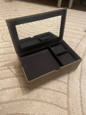 Smyckeskrin med spegel från Zara Home - Stilrent smyckeskrin i mockaliknande material i brungrå ton från Zara Home. Locket har en stor spegel på insidan och insidan har flera fack för smycken och accessoarer. Perfekt för att hålla ordning på dina favoriter. Får plats med mycket